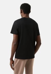 Czarny bawełniany t-shirt z krótkimi rękawami, okrągłym dekoltem, gładką fakturą i luźnym krojem, zestawiony z jasnobeżowymi spodniami.