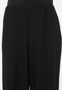 Μαύροι πλεκτοί παντελόνες με φαρδιά ζώνη μέσης και κάθετη υφή, προσφέροντας απαλό, ελαστικό ύφασμα με διακριτικές πιέτες.