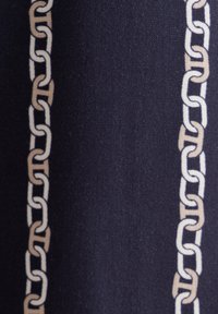 Tessuto navy con un motivo a catena ripetuto in beige e bianco, caratterizzato da anelli di catena interconnessi che creano un aspetto testurizzato.