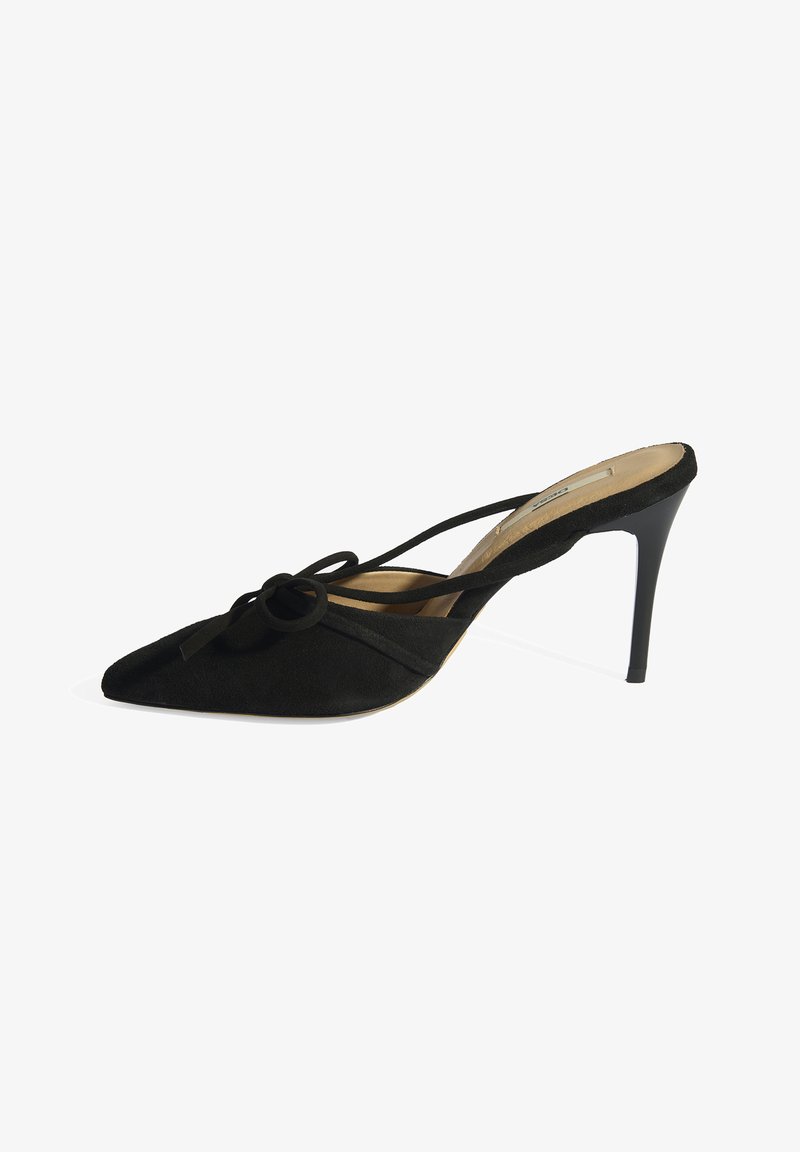 Zwarte suède hoge hak met spits toelopende neus, voorzien van een strikdetail in het midden en kruisbandjes. Lichtbeige binnenzool en zwarte stilettohak.
