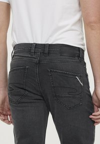 Donkergrijze spijkerbroek met een aansluitend ontwerp, voorzien van twee achterzakken, subtiele stikseldetails en een zwart leren logo label op de tailleband.