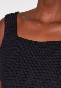 Primo piano di una persona che indossa un top in maglia nera texturizzata con spalline larghe, che mostra la pelle dalle spalle alla parte superiore del petto.