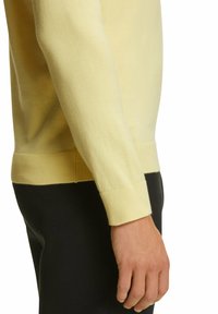 Maglione giallo chiaro realizzato in tessuto morbido, con scollo rotondo e polsini a coste. La manica è di lunghezza media e leggermente aderente.