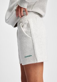 Lys grå shorts i bomullsblanding med elastisk midjebånd og sidelommer, med grønn brodert "CASPARA"-logo på kanten.
