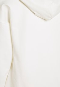 Sudadera blanca con una textura suave, corte relajado y capucha. Sin patrones visibles ni detalles de hardware. Diseño simple y limpio.