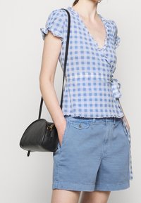 Top a quadretti blu e bianchi con maniche arricciate, abbinato a pantaloni corti azzurri e una piccola borsa nera con zip.