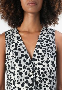 Abito senza maniche in bianco e nero con scollatura a V, caratterizzato da un motivo a pois, dettagli con bottoni davanti e tessuto testurizzato.