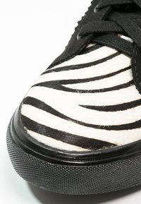 Gros plan sur la pointe d'une basket à rayures zèbre noires et blanches, avec des lacets noirs et une semelle en caoutchouc texturée noire.