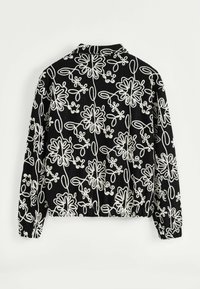 Veste noire à manches longues avec des motifs floraux abstraits blancs et des poignets élastiques, vue de dos sur fond blanc.