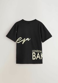Melna kokvilnas T-kreklu ar metāliski zeltītām grafiskām burtu uzrakstiem, "en" un "LONDON BAK," uz muguras. Īsām piedurknēm un apaļas kakla izgriezuma dizains.
