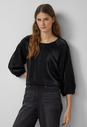 Black blouse with a soft, shiny texture, relaxed fit, and elbow-length sleeves. Paired with dark gray jeans, creating a monochromatic look.