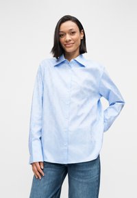 Világoskék gombos ing finom mintával, klasszikus gallérral és hosszú ujjakkal, kék farmernadrággal párosítva.
