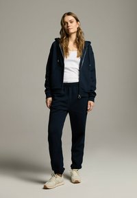 Granatowy hoodie i dopasowane dresy wykonane z miękkiego materiału. Hoodie posiada zamek błyskawiczny i kieszenie, zestawione z białymi sneakersami.