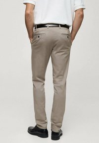 Béžové kalhoty s úzkým střihem, se dvěma zadními kapsami a hladkou texturou. Doplněné černými botami, pohled zezadu.