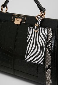 Sac à main noir texturé croco avec fermoir doré, étiquette rayée zèbre et panneau latéral à motif peau de serpent, doté d'une poignée supérieure.