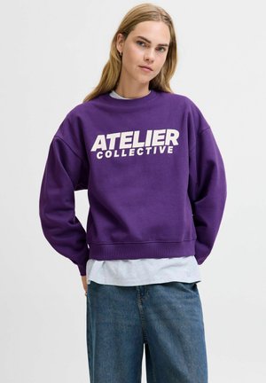 Lila Sweatshirt mit "ATELIER COLLECTIVE" in Weiß bedruckt. Hat einen lässigen Schnitt, Rippstrickbündchen und einen schichtartigen Stil mit einem grauen Hemd darunter.