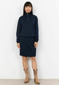 Navy zip-neck dress made of smooth fabric, featuring long sleeves and a fitted skirt. Worn with light brown ankle boots.