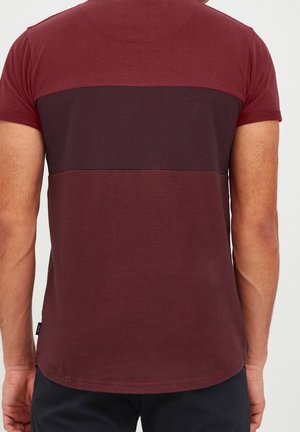 Maroon tričko s krátkým rukávem, které se vyznačuje horizontálním designem v barvách s texturovaným vzorem, má kulatý výstřih a rovný lem.