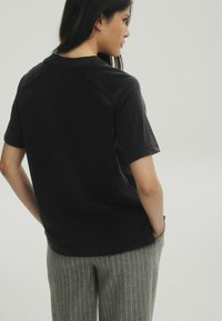Schwarzes T-Shirt mit kurzen Ärmeln und Rundhalsausschnitt, aus weichem Stoff. Mit einer lässigen Passform und leicht strukturierten Akzenten an den Schulternähten.