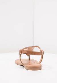 Kash tan leather yang memiliki strap belakang dengan gesper yang dapat disesuaikan, sol datar, dan desain yang sederhana. Bagian tempat kaki terlihat halus.