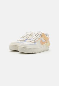 Zapatillas Nike en blanco y durazno con parte superior de cuero y sintético, puntera redondeada, suela de goma texturizada y detalles de cordones visibles.