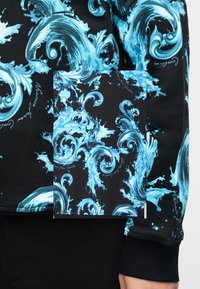 Μαύρο ύφασμα με μπλε και λευκό μοτίβο στροβιλισμένου νερού και διακοσμητικές καμπύλες, διακοσμημένο με μικρό καλλιγραφικό κείμενο.