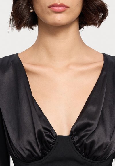 Abito in satin nero con profondo scollo a V e dettagli arricciati, elegante con maniche lunghe, che mette in risalto una texture morbida e una silhouette aderente.