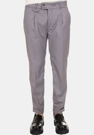 Pantaloni grigi su misura con pieghe frontali, chiusura con bottone e gambe affusolate. Abbinati a scarpe nere senza lacci per un contrasto.