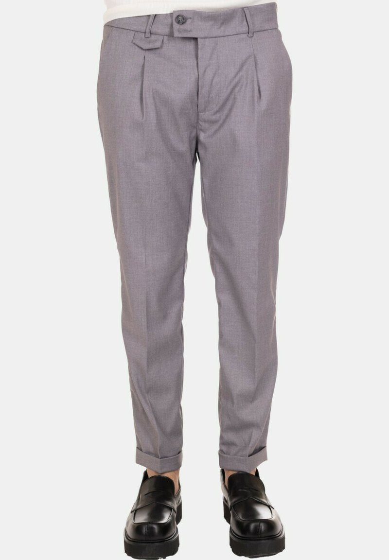 Pantaloni grigi su misura con pieghe frontali, chiusura con bottone e gambe affusolate. Abbinati a scarpe nere senza lacci per un contrasto.
