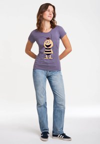Purple t-shirt featuring a cartoon bee design with black and yellow stripes. Paired with light blue jeans and navy sneakers.