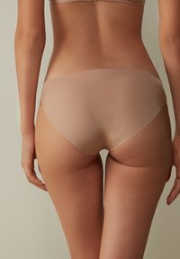 Beige nahtlose Unterwäsche mit glatter Textur, niedrigem Bund und subtilen Farbverlauf, mit einem geschwungenen Rückenschnitt für zusätzlichen Komfort.