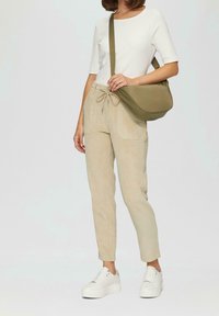 Ljusbeige kordflorsebyxor med dragskärm, kombinerat med en ribbad vit topp och en olivgrön crossbody-väska. Vita platåskor fullända looken.