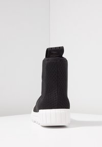 Černé vysoké tenisky s texturovanou síťovinou, bílou gumovou podrážkou a poutkem na zadní straně pro snadné obouvání.