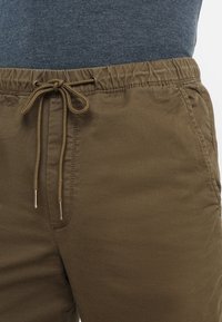 Mörk olivgrön lätta joggerbyxor med elastisk midja, justerbar dragsko och sidofickor. Slät tygtextur, avslappnad design.