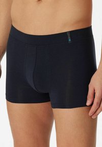 Black boxers made of soft material, featuring a wide waistband and a snug fit. The design includes a front pouch and subtle stitching details.