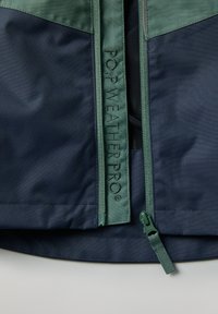 Marineblauwe en groene weersbestendige jas met een ritsluiting, voorzien van gestructureerde stof en het "P.O.P WEATHERPRO" logo op het ritspaneel.