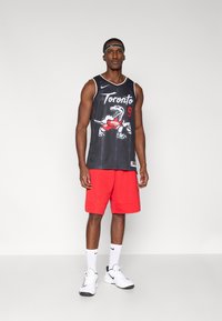 Čierny basketbalový dres s logom Toronto Raptors a číslom 9, v kombinácii s červenými šortkami a bielymi teniskami.