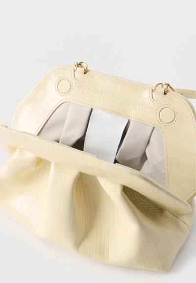 Μπεζ δερμάτινη τσάντα με υφή και χρυσό κούμπωμα, ανοιχτή για να δείξει εσωτερική επένδυση από μπεζ ύφασμα και δομημένο πλαίσιο.