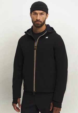 Black jacket with a zip front, featuring a hood, ribbed cuffs, and an emblem on the chest. Yellow accents along the zipper add detail.