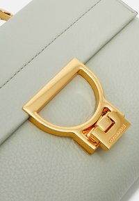 Vihreä nahkakäsilaukku, jossa on teksturoitu pinta, kultaiset tarvikkeet ja näkyvät tikit reunoilla.