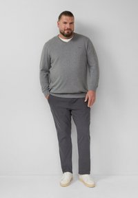 Grijze v-hals trui, donkergrijze broek en witte sneakers. Zachte texturen; minimalistisch ontwerp met een subtiele merkl logo op de trui.