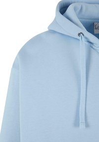 Helles blauer Kapuzenpullover mit weicher Textur, der ein einfaches Design, eine Kordel und ein kleines Metallösen an der Kapuze aufweist.