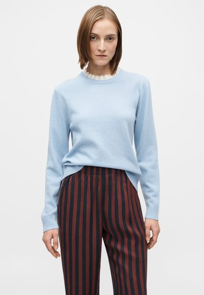 Hellblauer Pullover mit gerippten Bündchen und Ausschnitt, kombiniert mit bordeauxroten und marineblauen vertikal gestreiften Hosen mit elastischem Bund.