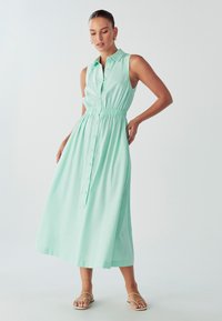 Mėtų žalios spalvos, be rankovių maksi suknelė su mygtukų priekiu, elastinga juosmens dalimi ir apykakle. Minkšta medžiaga su lygia tekstūra. Paprastas dizainas.
