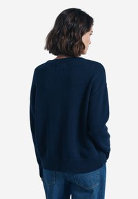 Maglione a maglia blu navy con scollatura a girocollo, orlo e polsini a coste, vestibilità rilassata e tessuto texturizzato, mostrato dal retro.