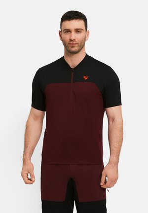 Man with short dark hair wearing a black and maroon short-sleeve cycling jersey and matching shorts, standing against white background.