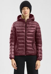 Burgunderfarbene Pufferjacke mit horizontalem Steppmuster, Frontreißverschluss, Kapuze und Seitentaschen; glänzende Stoffoberfläche. Schwarze Strickmütze getragen.
