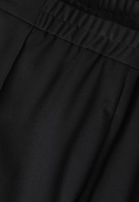 Tessuto nero con una superficie liscia e una cintura arricciata. La vista ravvicinata mette in evidenza la morbidezza e la sottile lucentezza del materiale.