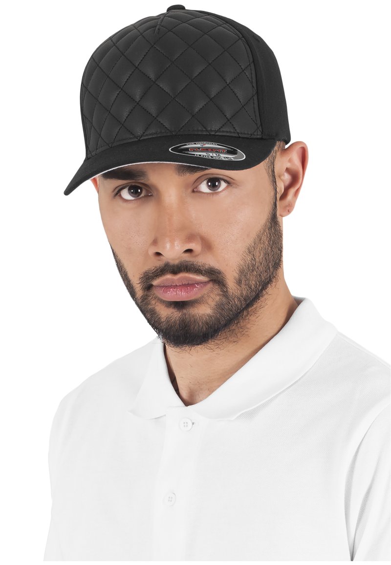 Cappello trapuntato nero con corona piatta e visiera rigida, indossato da un individuo in una polo bianca, che mette in mostra il materiale testurizzato e la forma.