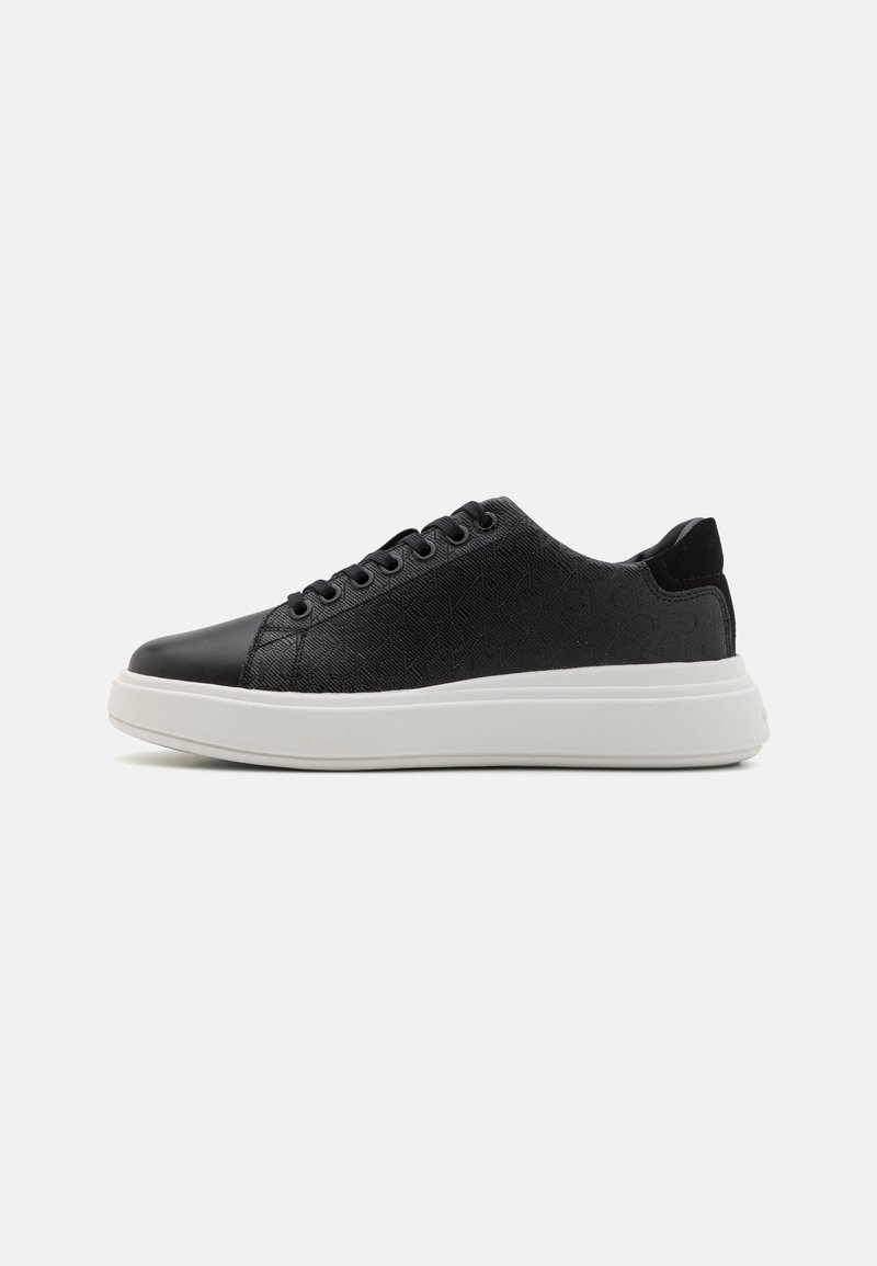 Baskets noires en matériau texturé avec un bout en cuir lisse. Elles comportent une semelle blanche, une fermeture à lacets, et un motif subtil sur la tige.